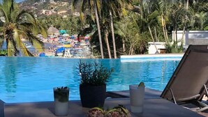 Vista a la piscina con una playa despejada, palmeras y un pueblo lejano.