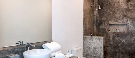 A modern bathroom with a large white sink, a toilet, and a shower area with a textured wall.