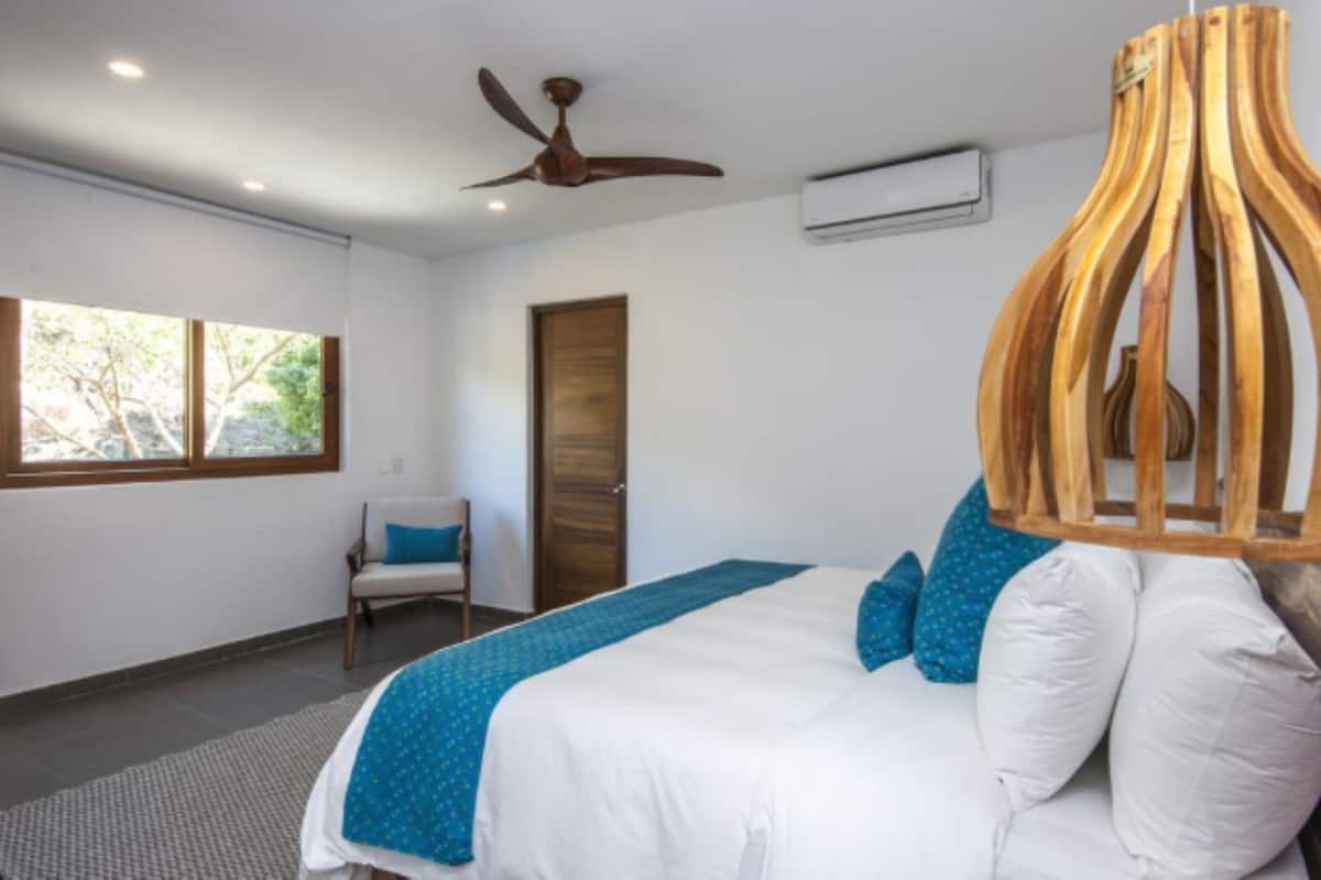 Un dormitorio con una cama, un ventilador de techo, una escultura de madera y una ventana.