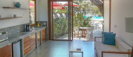 A modern kitchen with a built-in dishwasher, wooden cabinets, and a large sliding glass door leading to an outdoor seating area with a pool and umbrellas.