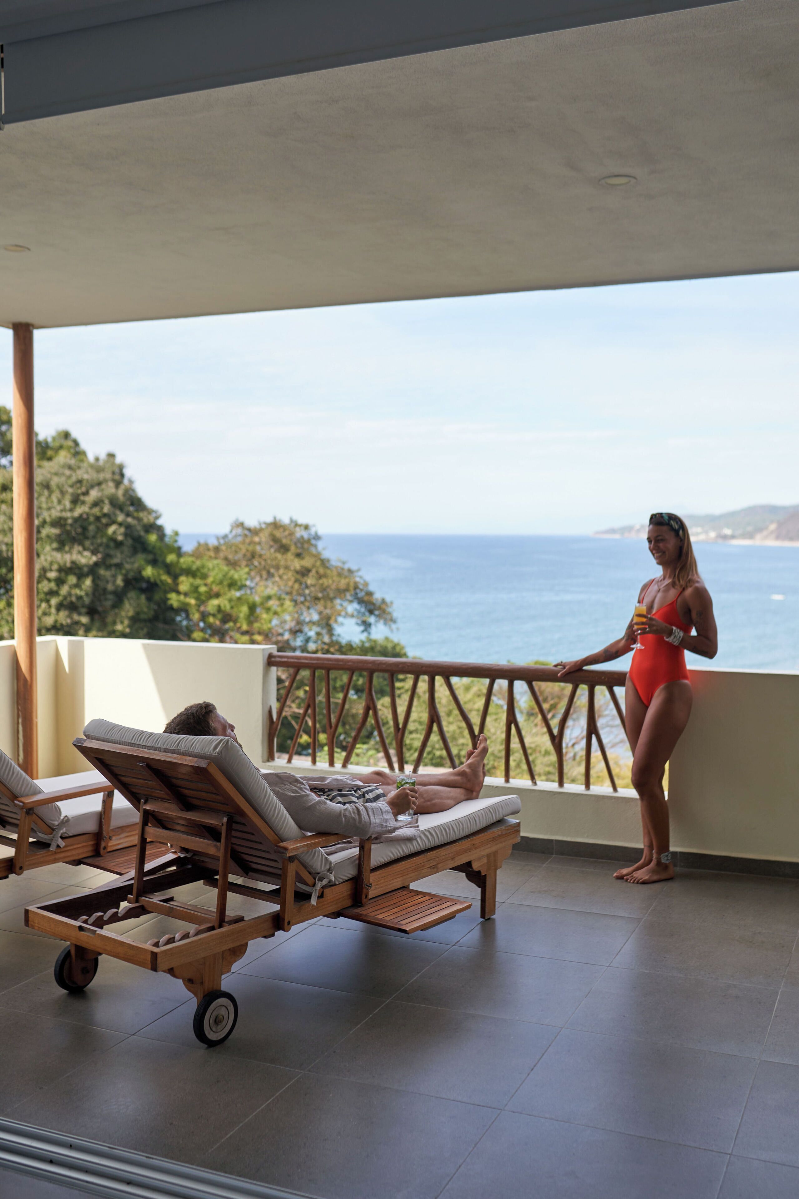 A balcony with a view of the ocean, a lounge chair, and a wooden cart.