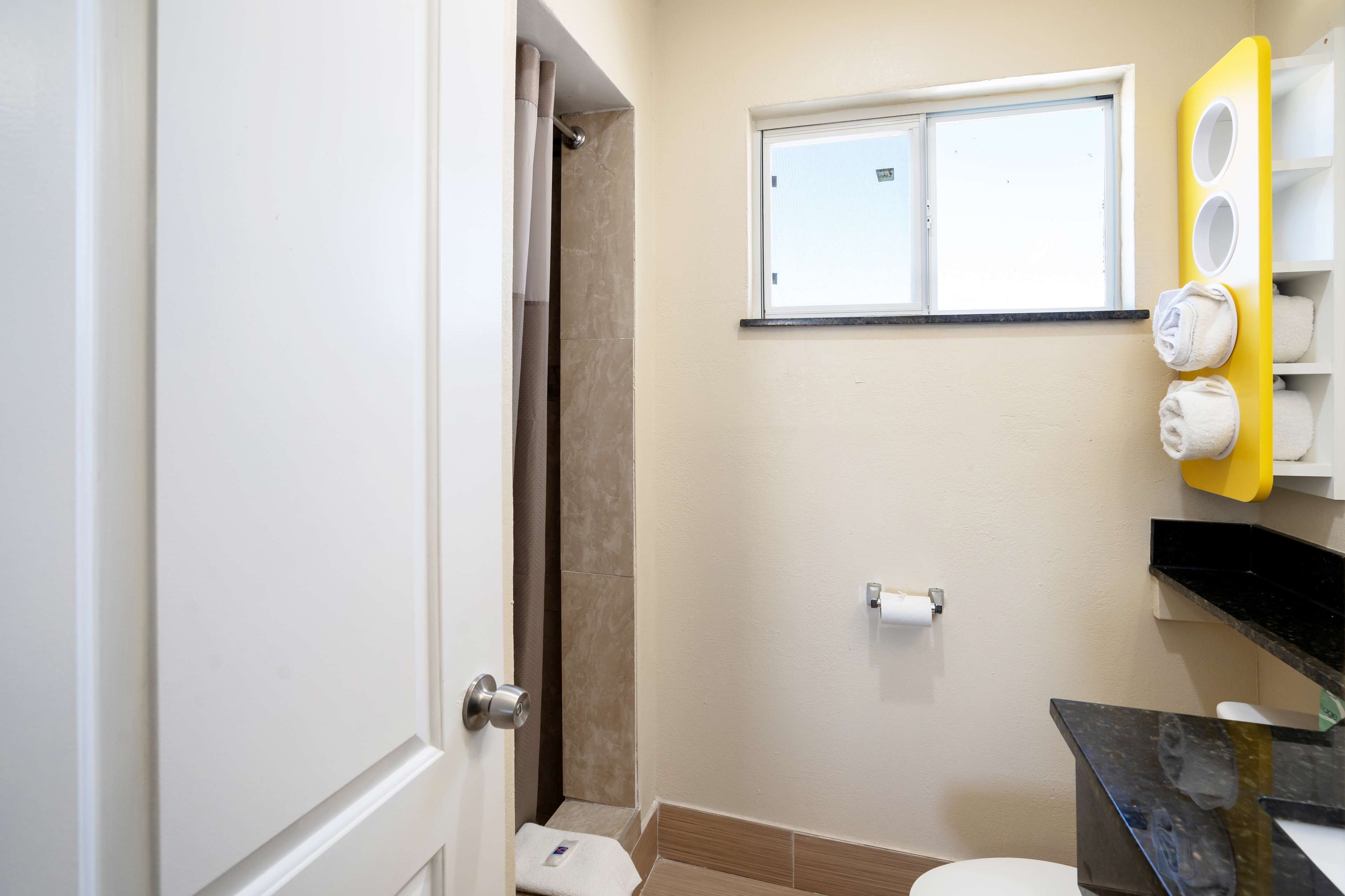 Un bagno con il water, una doccia, un portascopevoli con asciugamani, una finestra e un lavandino con uno specchio.