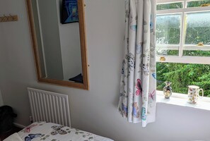 Ein Schlafzimmer mit Bett, Heizkörper, einem fenster mit Vorhängen und Blick auf Grünfläche.