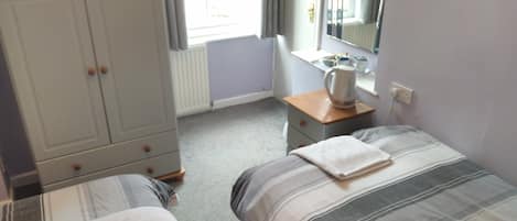 A bedroom with two beds, a wardrobe, a desk with a kettle, and a window with curtains.