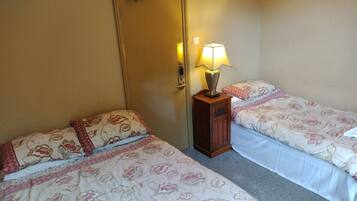 A hotel room with two single beds, each with floral-patterned bedding. There is a wooden nightstand with a lamp between the beds.