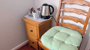 A wooden chair with a green cushion, a wooden nightstand with a kettle and a cup holder, and a white wall. - The Bull (Birmingham)