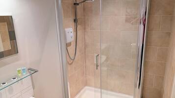 Eine begehbare Dusche mit Glaswänden, einer Handbrause, einer Bedienkonsole und einem Glasregal für Toilettenartikel.