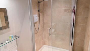 Une douche fermée par des parois de verre, dotée d’un pommeau de douche à main, d’un panneau de commande et d’une étagère en verre pour les articles de toilette.