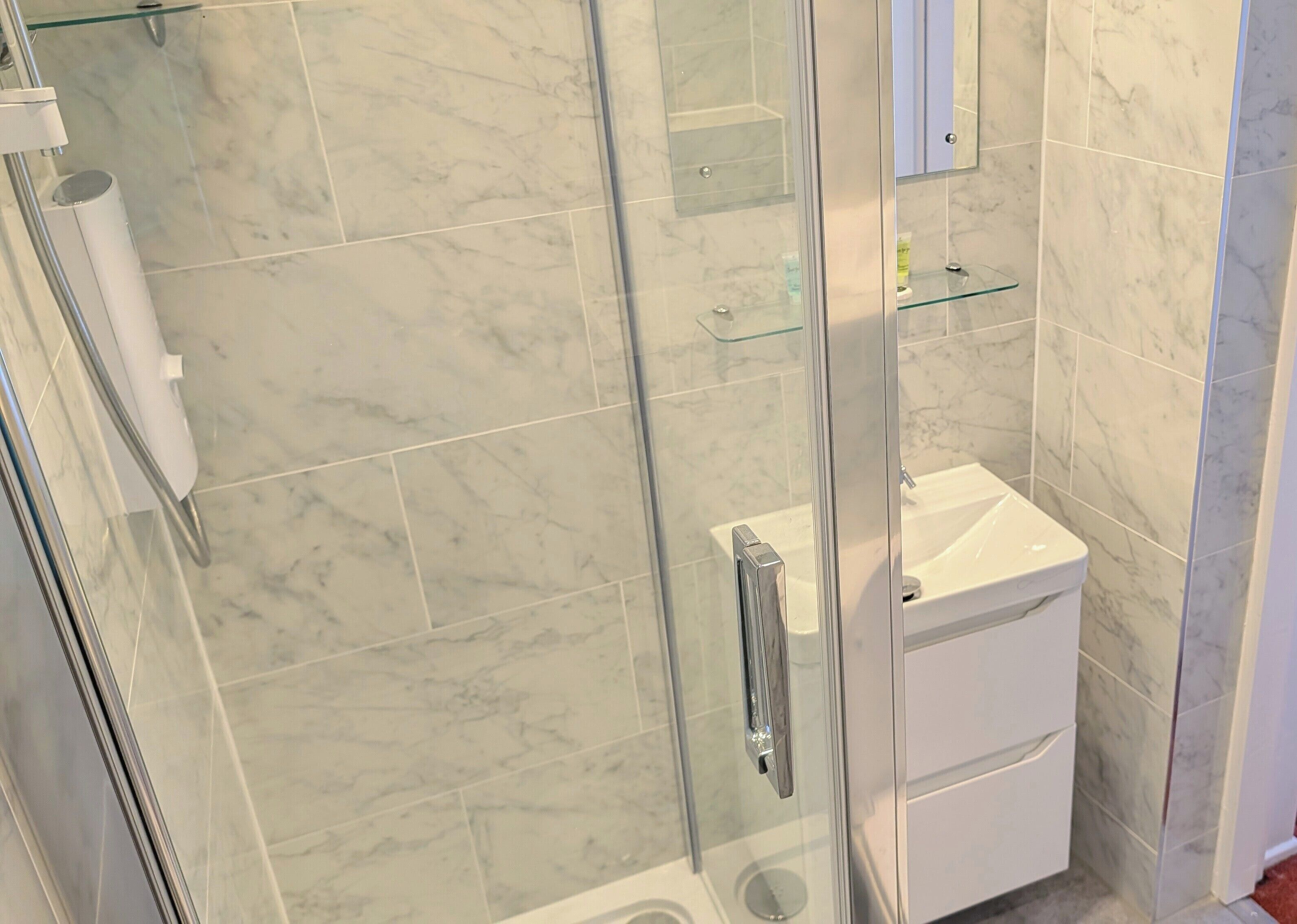 Un bany amb plat de dutxa de vidre, un lavabo blanc i un vàter.