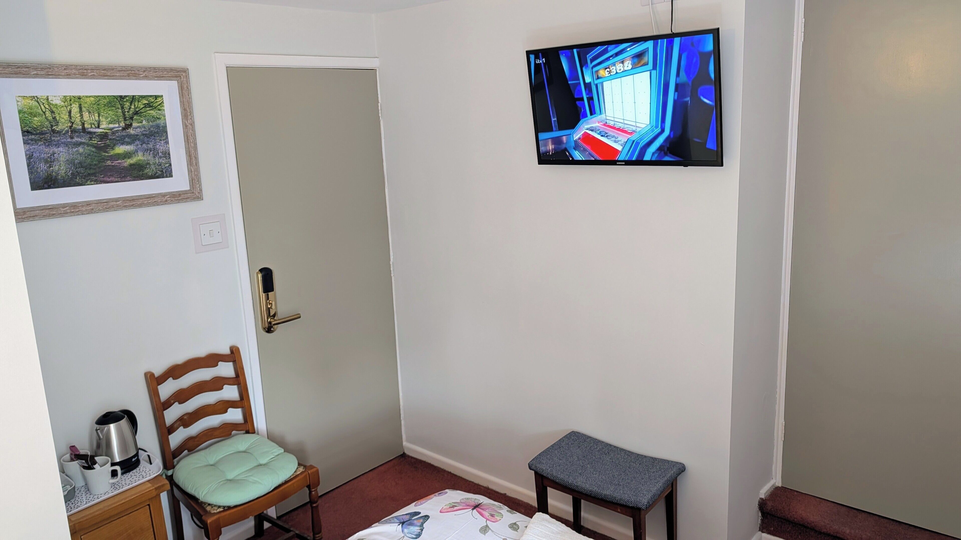 Una habitación con cama, sillón, mesita, televisor, puerta y un cuadro en la pared.