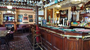 A bar area with a wooden counter, multiple stools, and a variety of bottles and glasses. - The Bull (Birmingham)