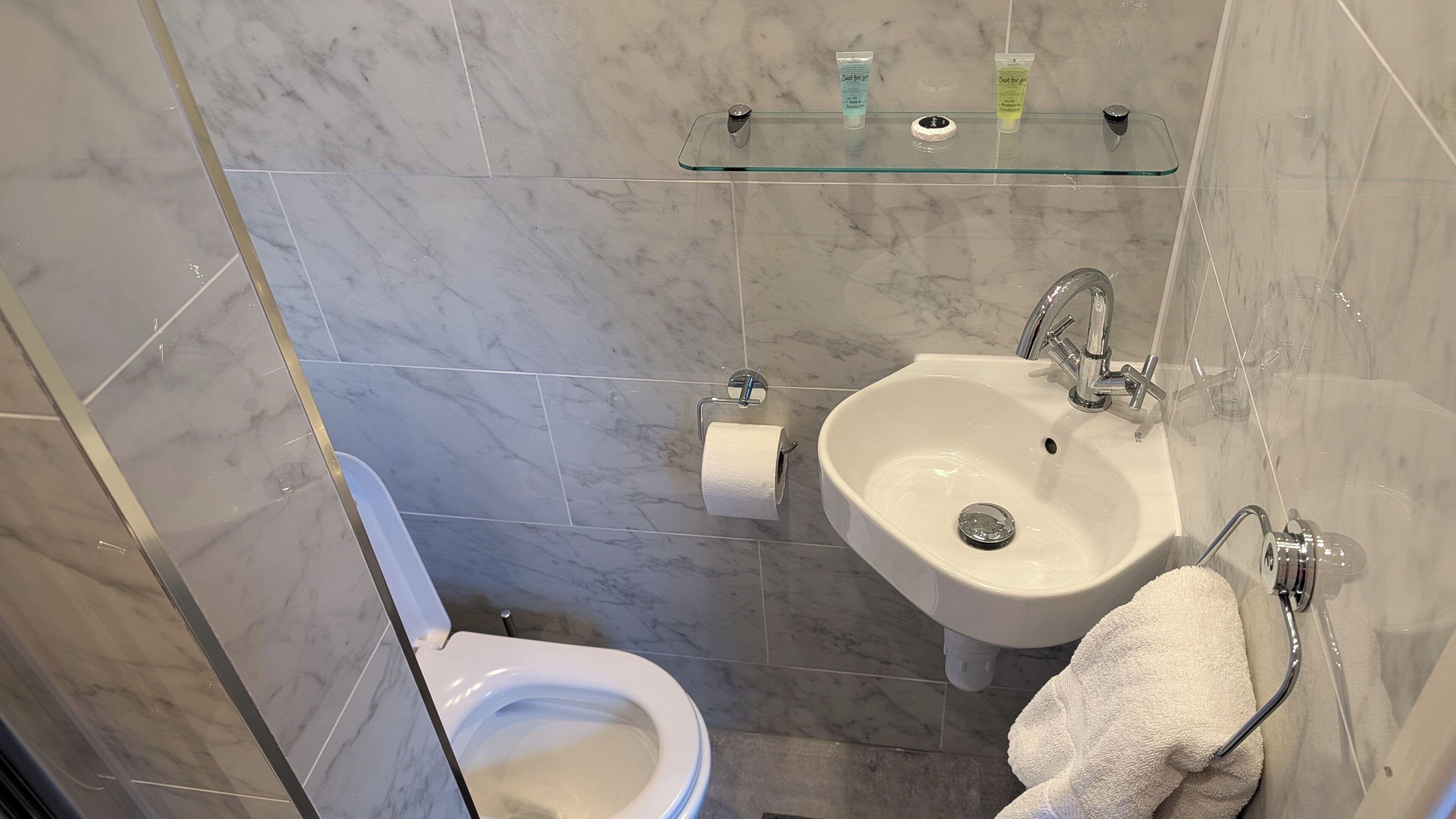 Een badkamer met toilet, wastafel en een glazen plank met toiletartikelen.