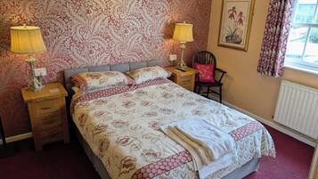 A bedroom with a bed, two bedside tables with lamps, a chair, a radiator, and a window with curtains.