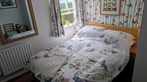 A bedroom with a bed, a radiator, a window with curtains, a mirror, and a wall with butterfly wallpaper. - The Bull (Birmingham)