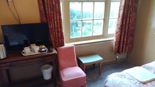 Une chambre d’hôtel équipée d’une télévision, d’une petite table, d’une chaise et d’une fenêtre avec des rideaux.