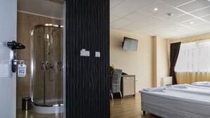 Una habitación de hotel con ducha, cama, escritorio y televisor.