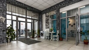 Amplia habitación con un amplio ventanal corredero que da a un aparcamiento. Hay una lavadora, una mesa con sillas y varias plantas en macetas.