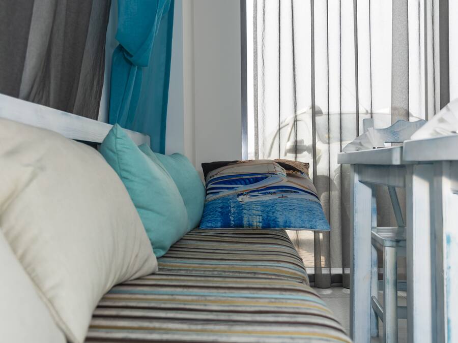 A bed with striped bedding and pillows, a bedside table with a tissue box, and a window with vertical blinds.