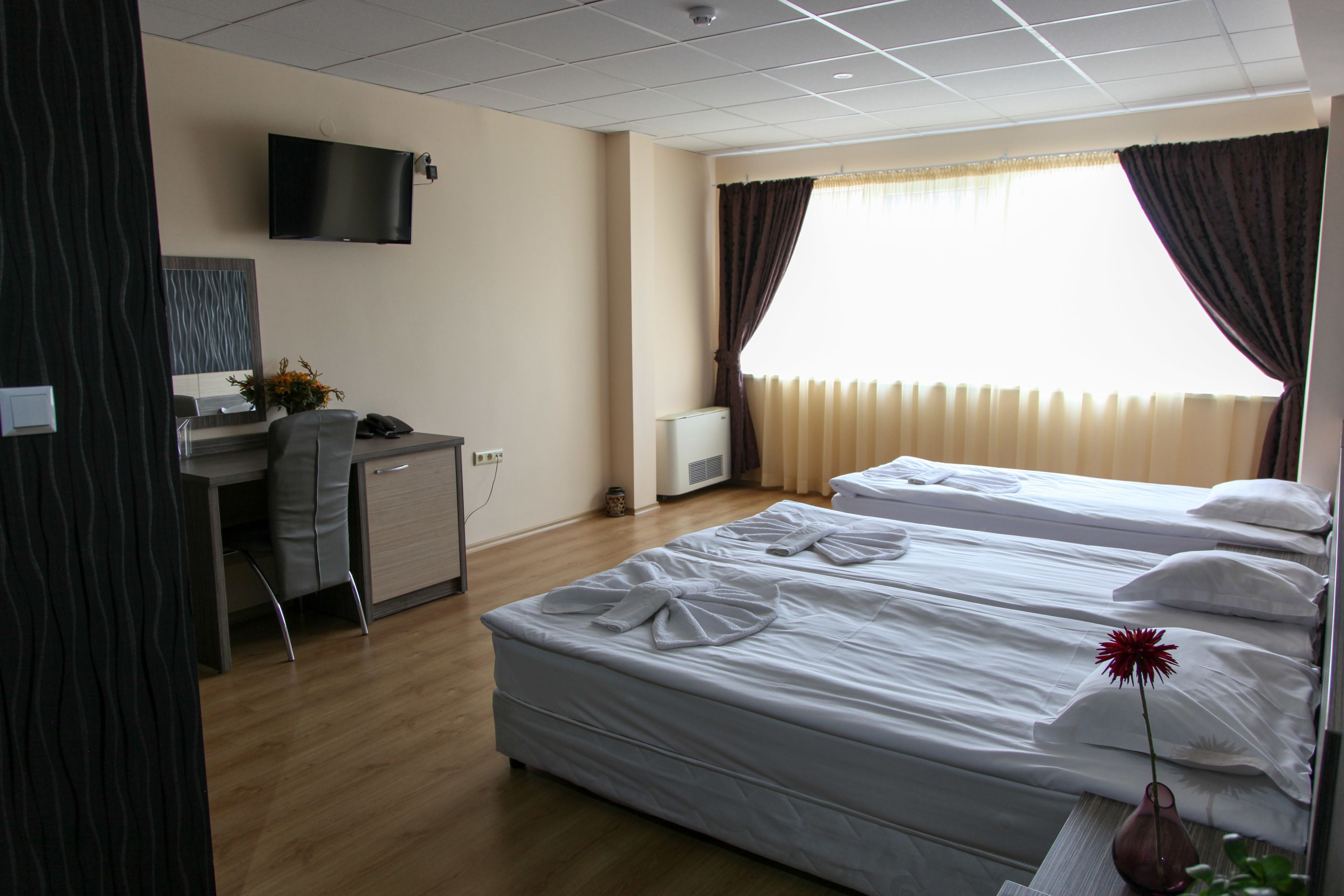 Habitación de hotel con dos camas, un escritorio, una silla, un televisor montado en la pared y una ventana con cortinas.
