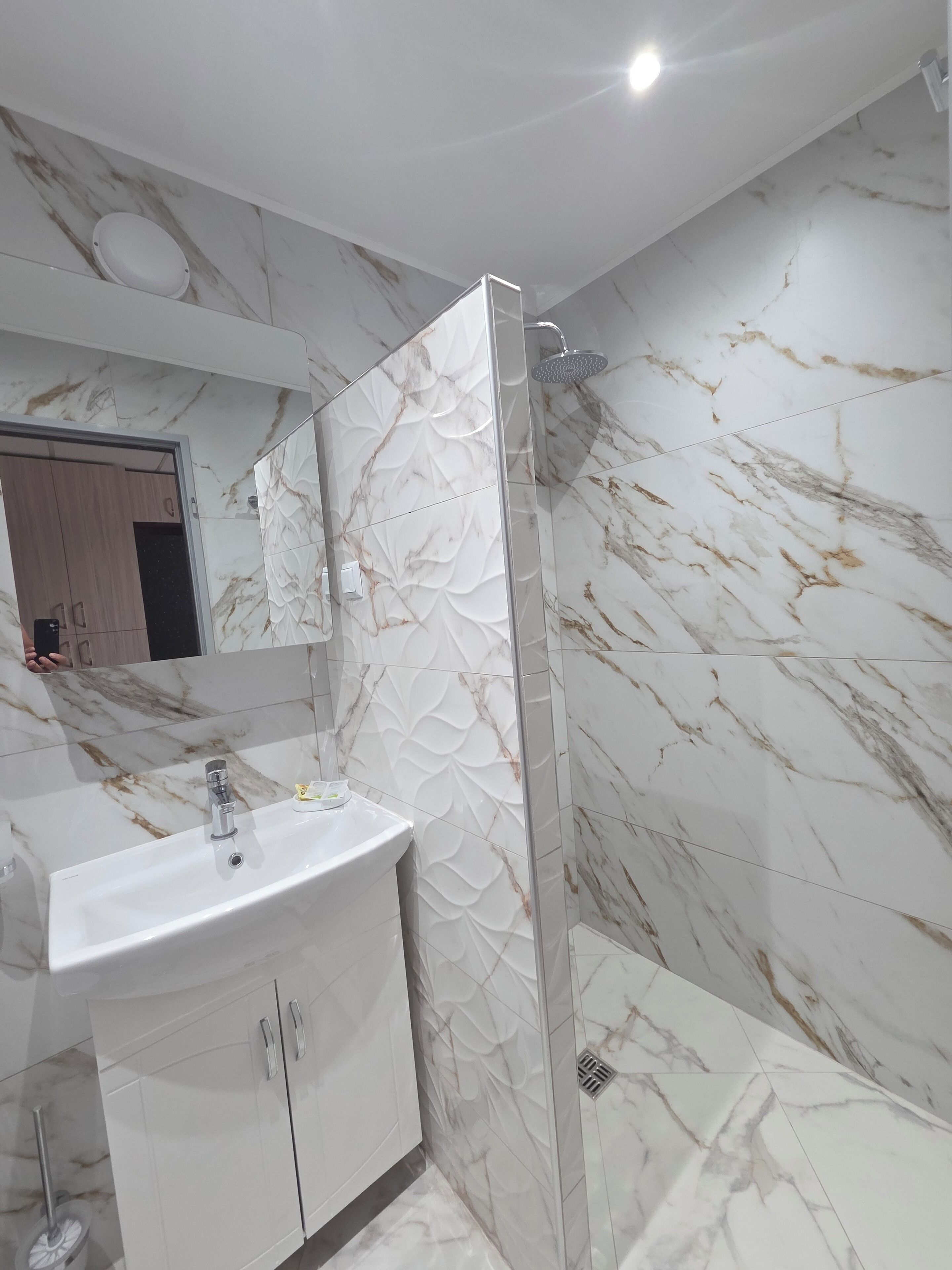 Un baño moderno con salpicadero de mármol, cabina de ducha y tocador con lavabo y armarios.