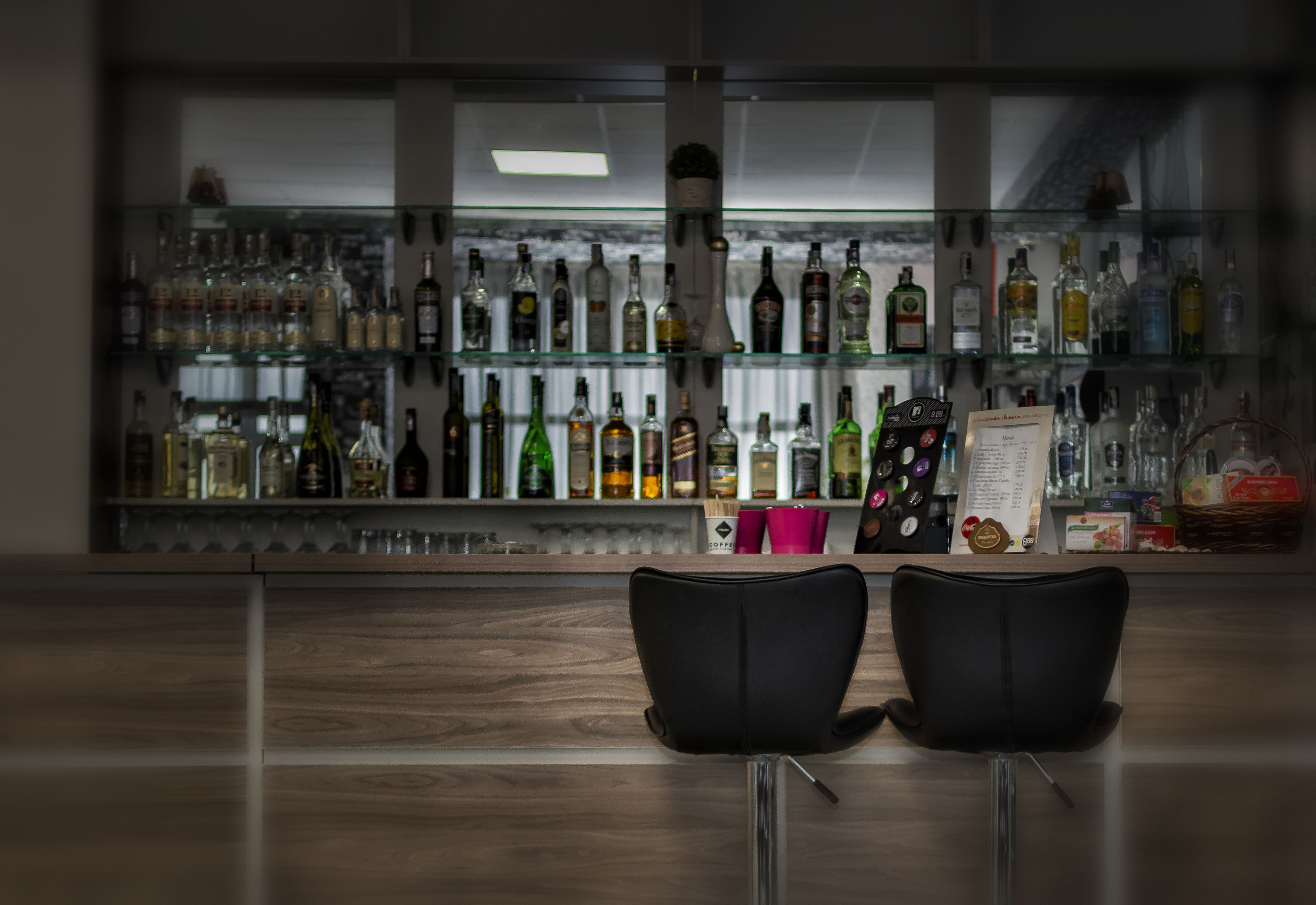 A bar area with two black chairs, a glass display shelf with various bottles, and a menu stand.