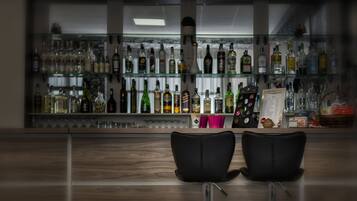 A bar area with two black chairs, a glass display shelf with various bottles, and a menu stand.
