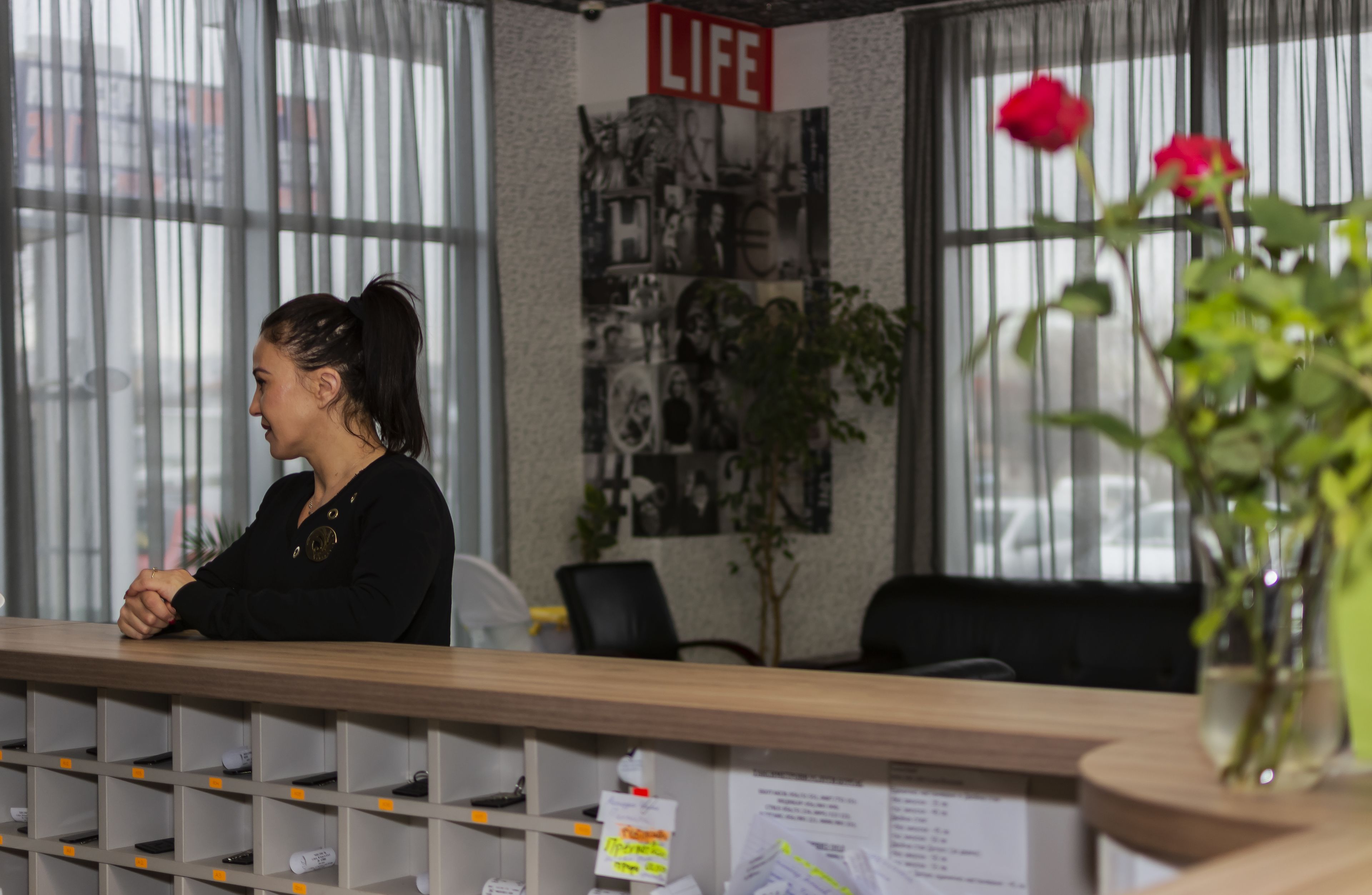 Una recepción con un letrero que dice 'LIFE', un tablón de anuncios con fotografías y una planta en maceta con una rosa roja.
