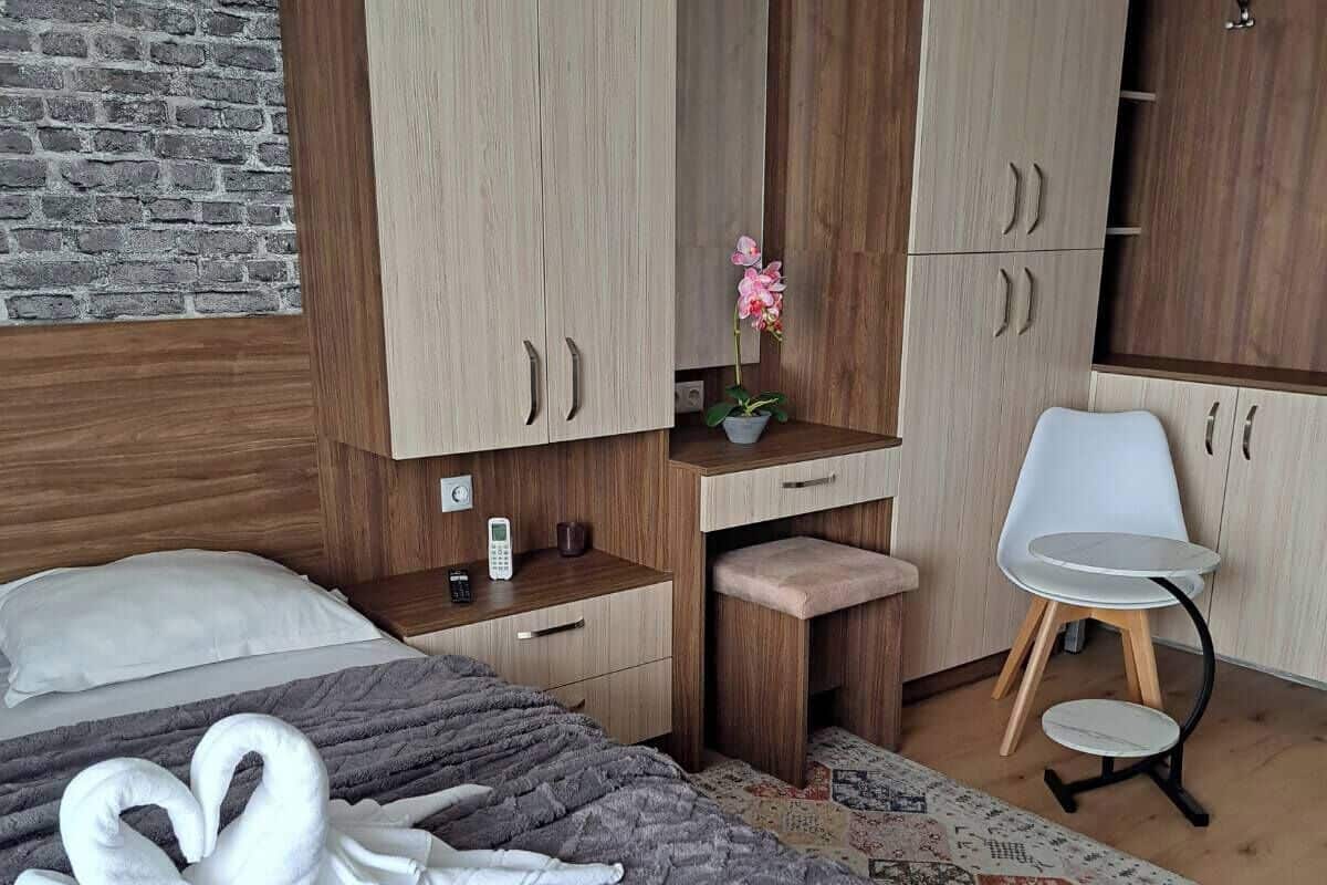 A hotel room with a bed, a desk, a chair, and wooden cabinets.