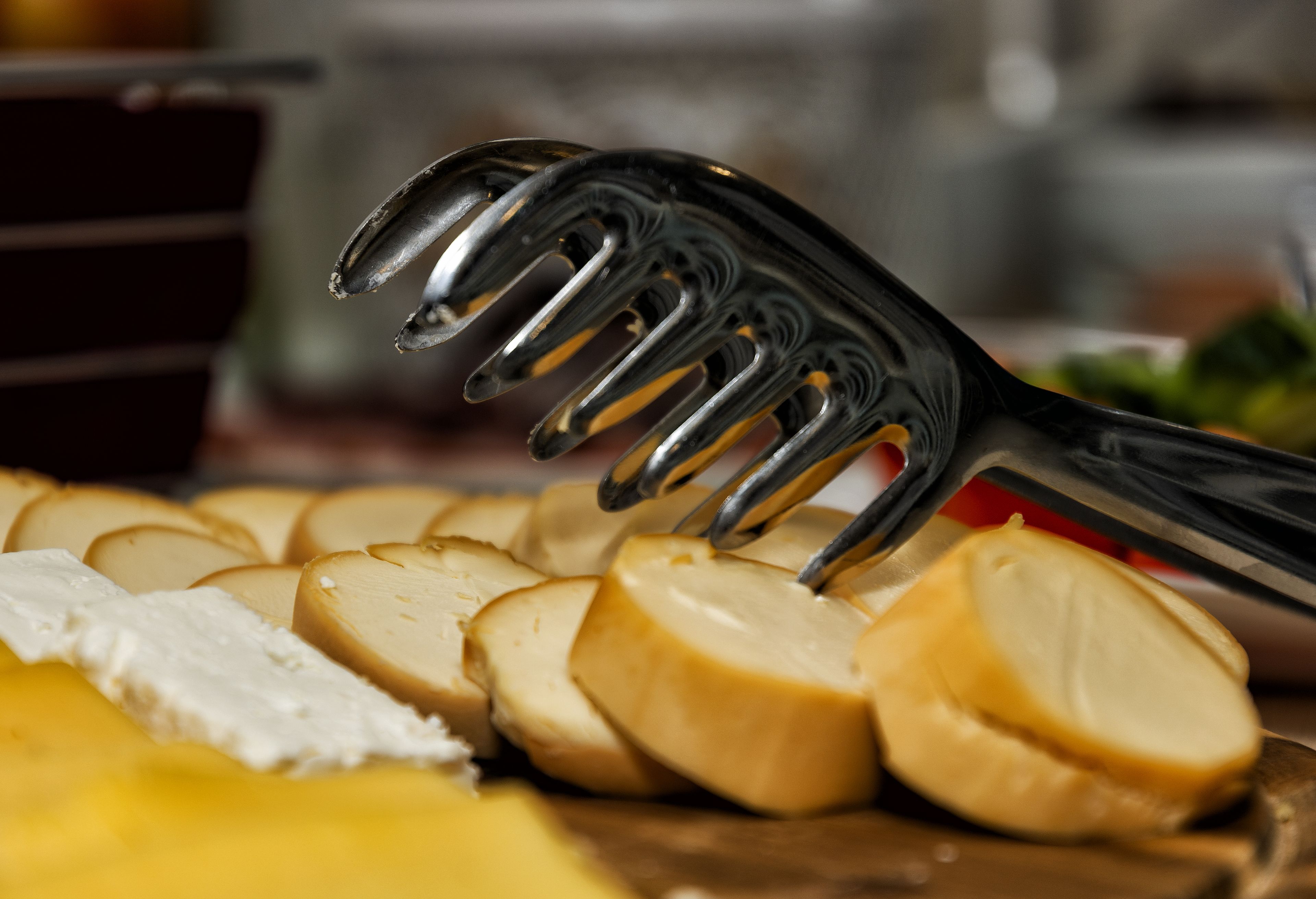 Une fourchette au design original, posée sur une surface en bois, à côté de tranches de fromage et d’une sorte de pâte à tartiner blanche.