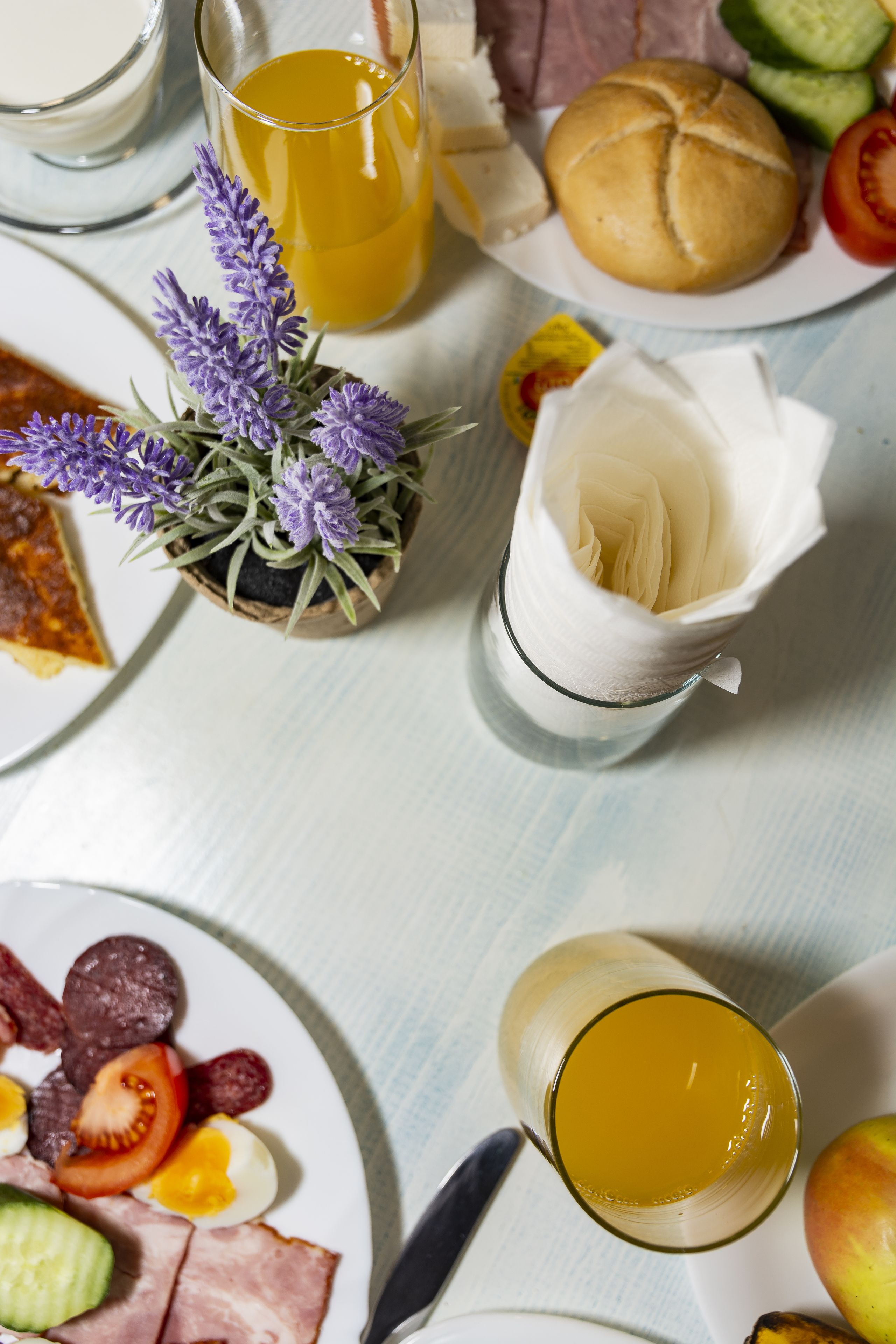 Ett frukostbord med tallrikar fyllda med mat, ett glas apelsinjuice och en liten krukväxt.