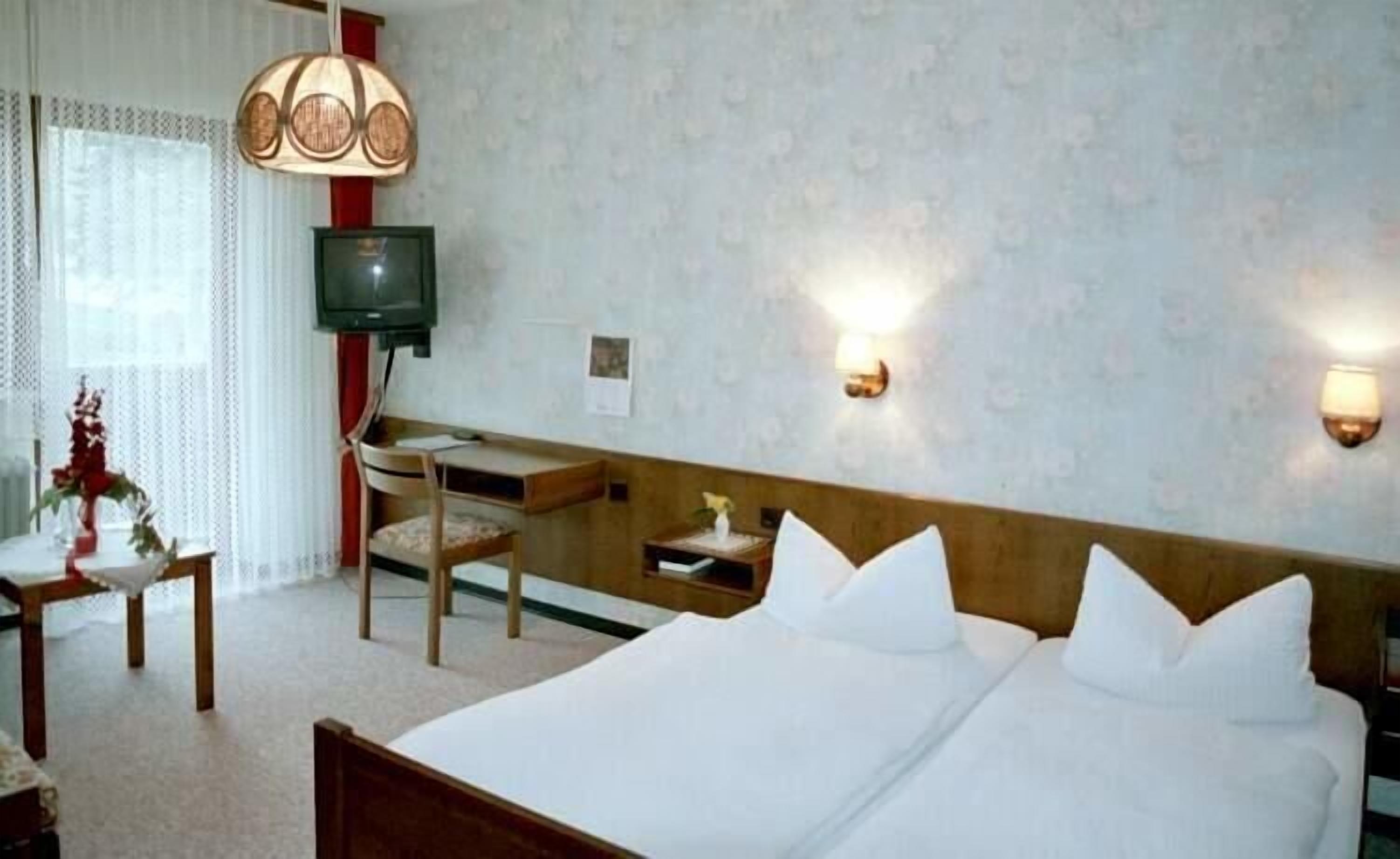A hotel room with a bed, desk, chair, TV, and wall-mounted lights.