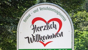 Une pancarte avec les inscriptions « Herzlich Willkommen » et « Finkenbach », placée dans un jardin.