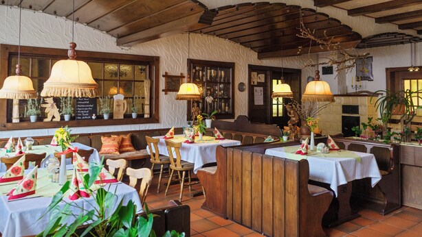 Un restaurant avec des tables et des bancs en bois, des lampes suspendues et des plantes en pot.