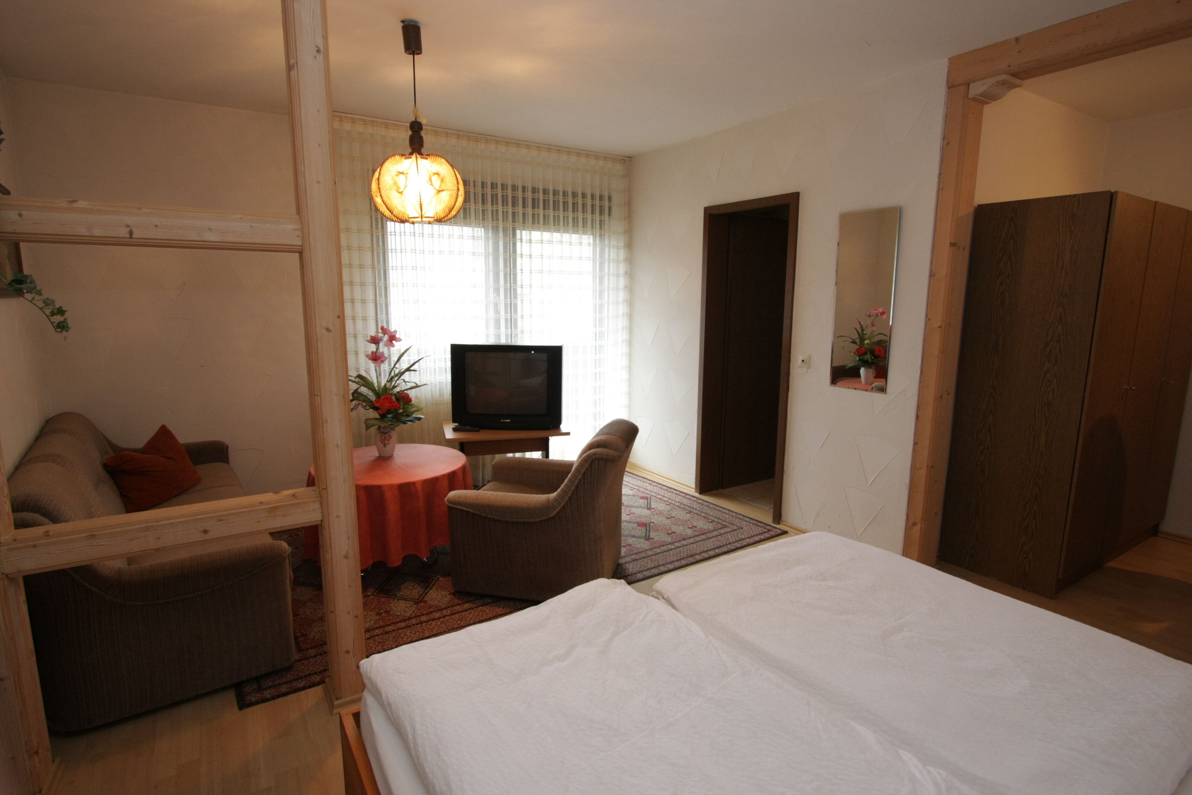 Een hotelkamer met een bed, een televisie, een bank, een stoel en een tafeltje met een bloevas.