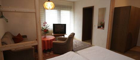 A hotel room with a bed, a TV, a sofa, a chair, and a small table with a flower vase.