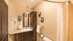 Une salle de bain avec un meuble-lavabo en bois, un évier, un miroir, un porte-serviettes et un rideau de douche.
