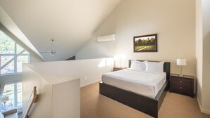 Une chambre à coucher comprenant un lit, des tables de chevet, un ventilateur de plafond, un climatiseur et une fenêtre donnant sur un paysage verdoyant.