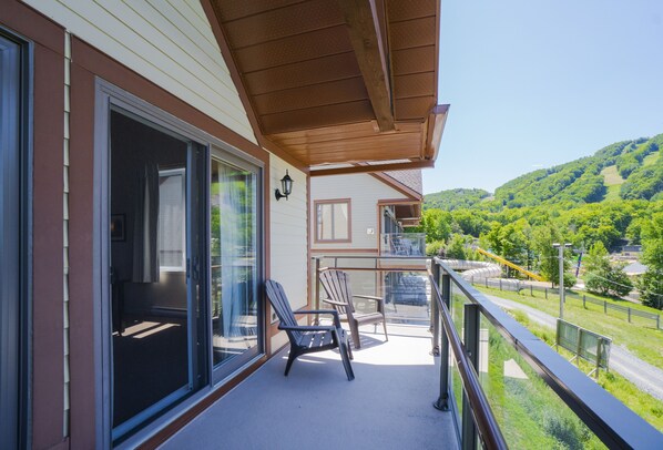 Un balcón con vista a una ladera verde, una pérgola de madera y dos sillas Adirondack.