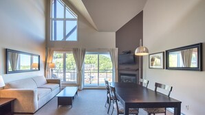 Un salon moderne comprenant un canapé, une table à manger avec des chaises, une cheminée et de grandes fenêtres donnant sur un paysage verdoyant.