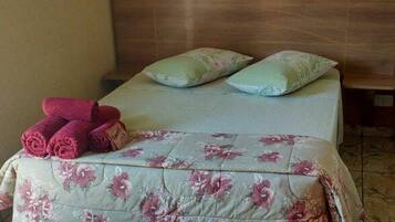 Una cama con ropa de cama floral, dos almohadas y toallas enrolladas sobre un suelo de baldosas.