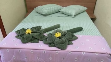 Cama bem arrumada com almofadas verdes e um edredom rosa.
