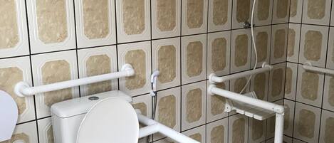 Un baño con inodoro, barras de apoyo, ducha y cubo de basura.