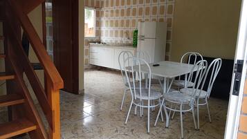 Una cocina con piso de baldosas, un refrigerador blanco, un lavamanos y una mesa de comedor con sillas.