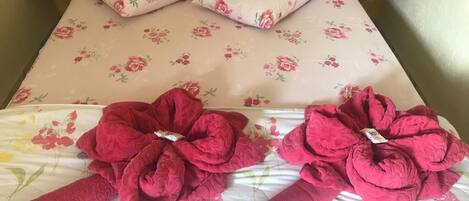 Ein Bett mit floraler Bettwäsche und zwei zusammengerollten Handtüchern darauf.
