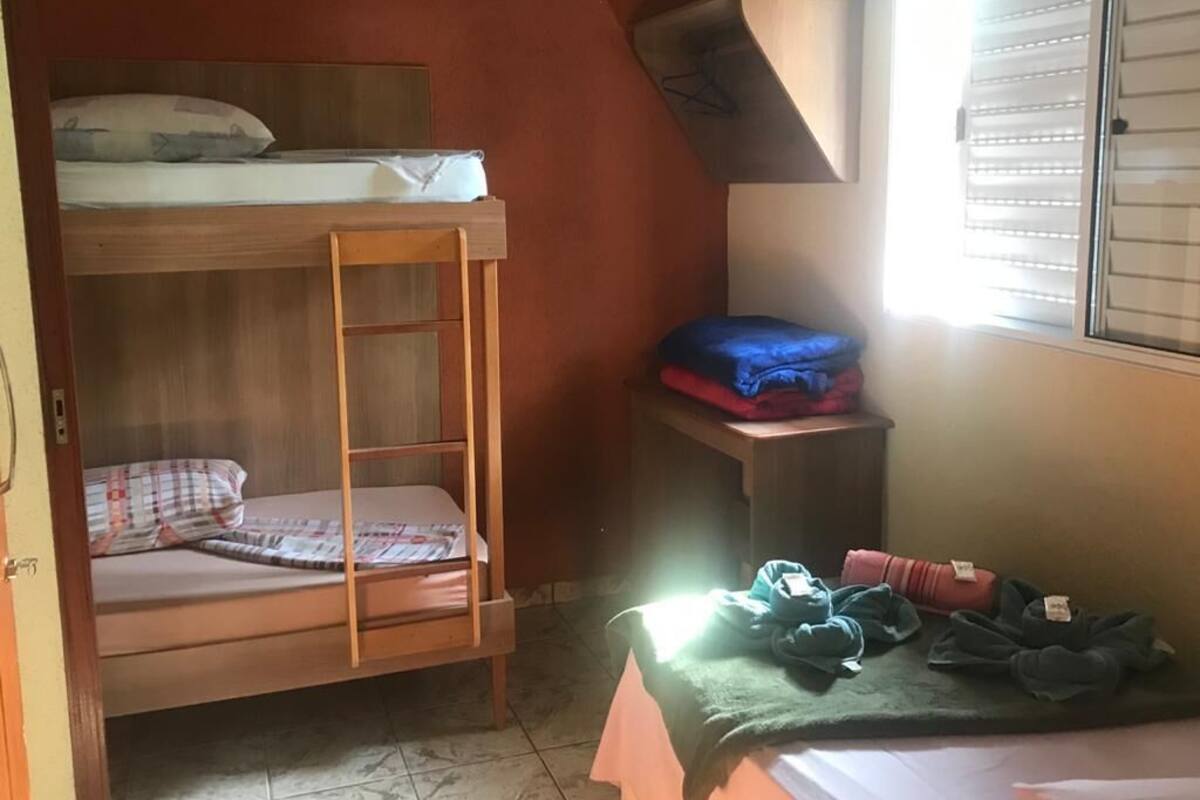 Een studentenkamer met een stapelbed, een bureau en een raam met zonwering.