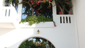 A white building with an arched entrance, potted plants, and red flowers. - Michalis Villas (Chania)