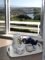 Una bandeja con tetera, tazas y azucarero en un balcón con vistas a un paisaje pintoresco.