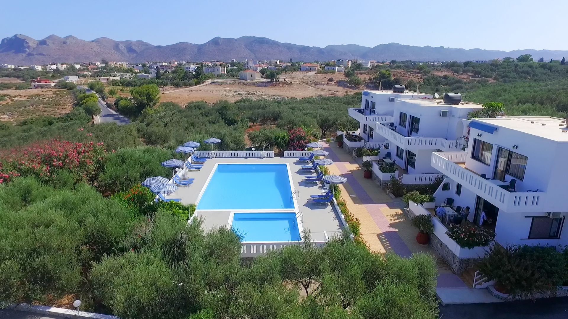 A resort with a large swimming pool, multiple lounge areas, and a view of the surrounding landscape.