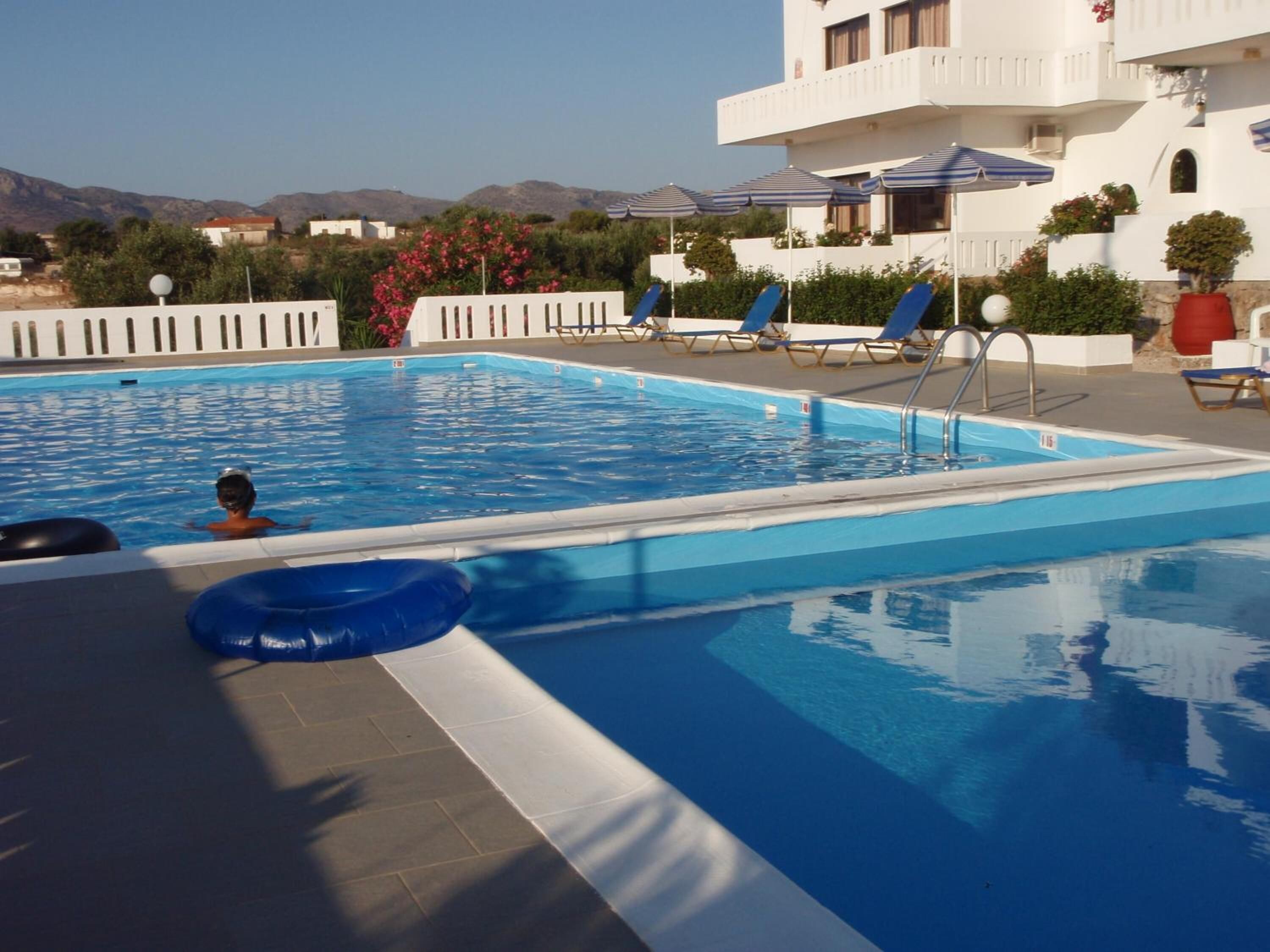 A swimming pool with lounge chairs and umbrellas, surrounded by a white building with balconies.