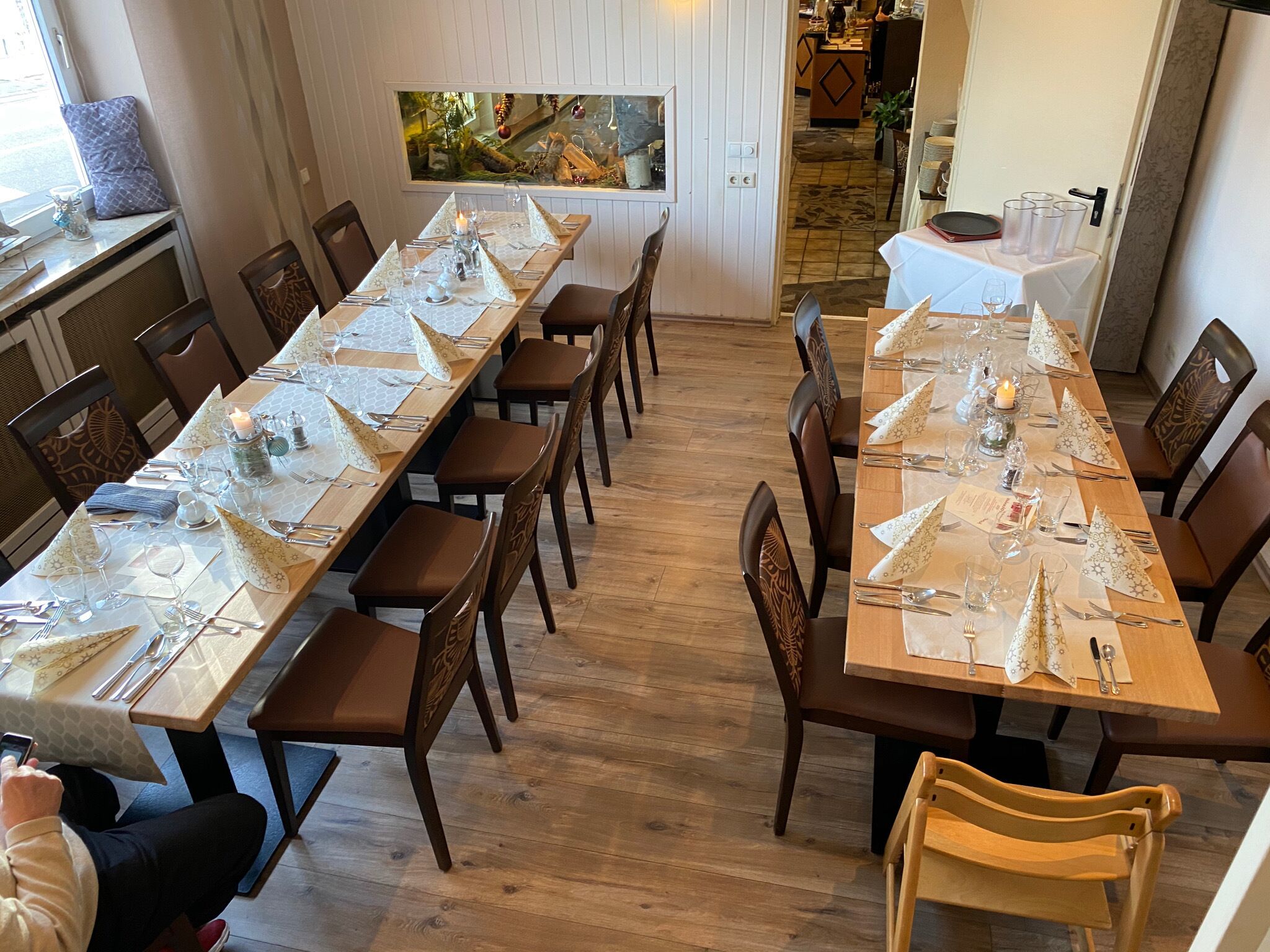 Un comedor con mesas largas dispuestas para una comida, sillas de madera y una pared decorativa con un cuadro.